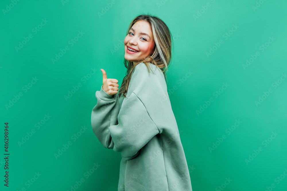 On a green background, an attractive girl shows okay. She smiles at the camera On a green background, an attractive girl shows okay. She smiles at the camera