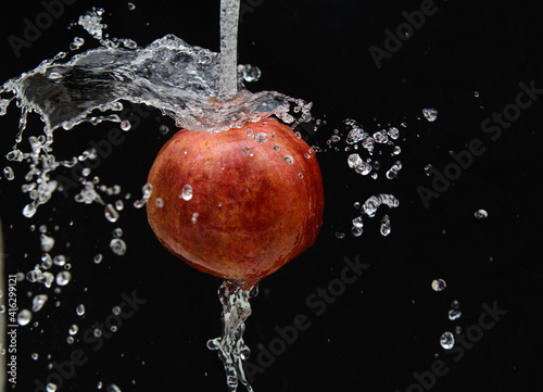 On a black background, a pomegranate fruit falls on a jet of water. Drops on a black background. Concept-fruit diet, vitamins
