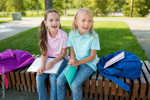 Two cute pupils girls having fun after lessons in the schoolyard in sunny day. Children playing and laughing. Schooldays with friends. 