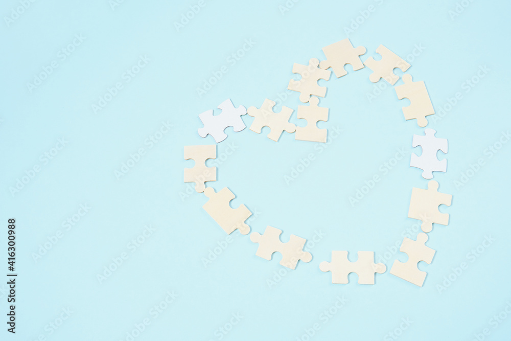 wooden puzzle pieces are laid out in the shape of a heart on a light blue background copy space