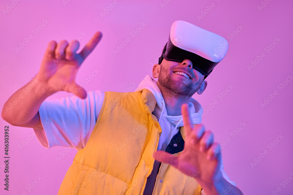 Young attractive smiling man in casual clothes, uses virtual reality glasses, making a frame gesture with his hands isolated on neon pink background. Future technologies. Young attractive smiling man in casual clothes, uses virtual reality glasses, making a frame gesture with his hands isolated on neon pink background. Future technologies.