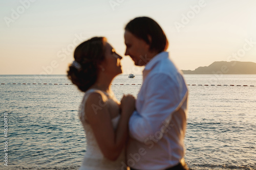 The bride and groom hug on the picturesque seashore, blurred couple © Nadtochiy