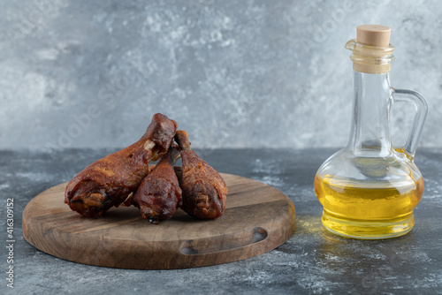 Grilled chicken legs on wooden board with glass of oil over grey background photo