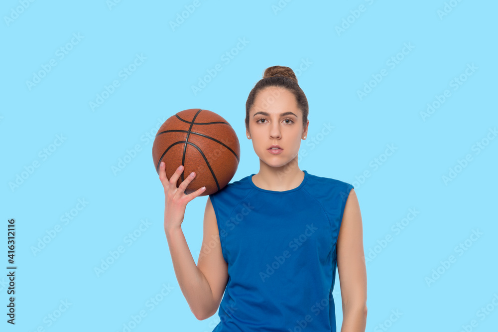 Beautiful caucasian girl looking at camera and holding basketball isolated on blue background.