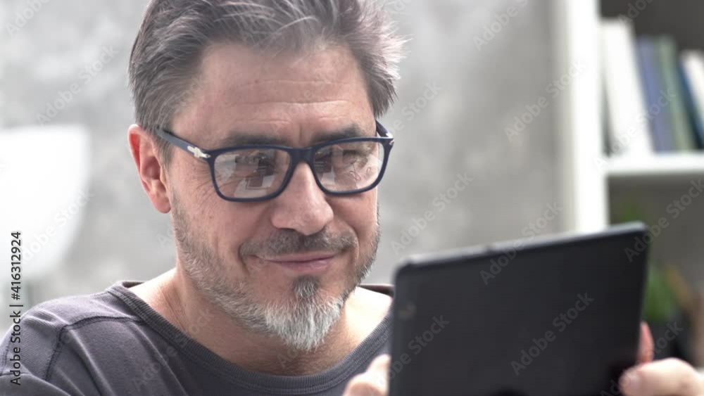 Man using tablet computer at home. Working at home, chatting, posting or browsing the internet and social media. Portrait of mature age, middle age, mid adult man in 50s. Man using tablet computer at home. Working at home, chatting, posting or browsing the internet and social media. Portrait of mature age, middle age, mid adult man in 50s.