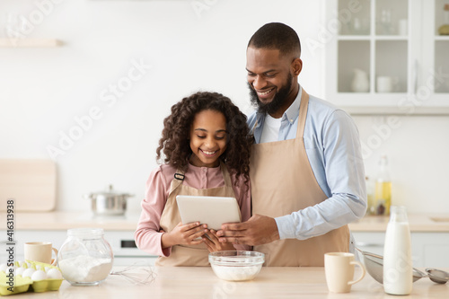 Black man and girl cooking in the kitchen reading recipe