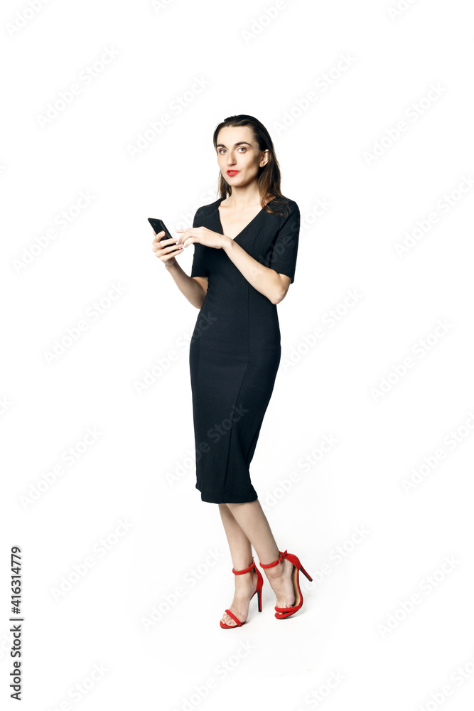 Business woman (fatal woman) in a black dress with red lipstick looks to the camera holding a smartphone, isolated on a white background. Business woman (fatal woman) in a black dress with red lipstick looks to the camera holding a smartphone, isolated on a white background.