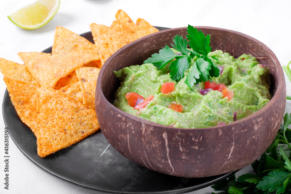 Guacamole dip in a wooden bowl and nacho chips. Mexican food