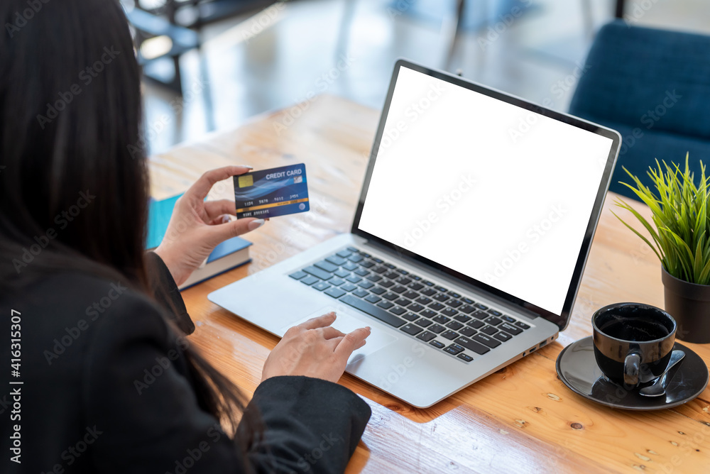 © amnaj - Close up of woman hand holding a credit card and using the laptop at the office. Mock up.
