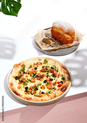 Olives and Tomato Focaccia and Cornbread on white table. White table and monstera palm leaves in sunlight with hard shadow. Summer day food concept.