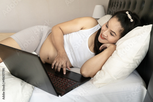 Pregnant mother use a computer for online shopping on the bedroom. She smile and very happy to see the baby.