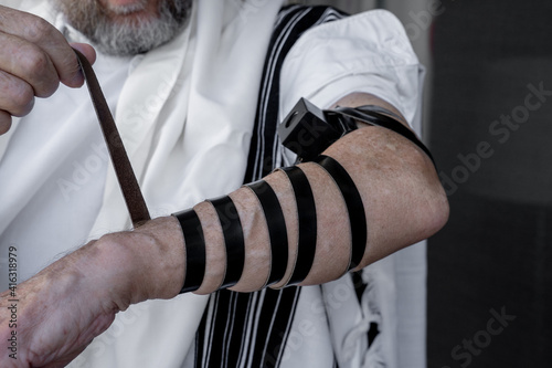 Religious jew dressed in a tallit puts tefillin on his left hand (264) © Maayan