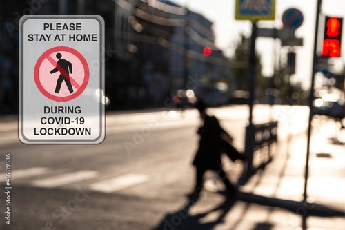 Concept ''Please stay at home during COVID-19 lockdown'' road sign against a defocused walking man in the city