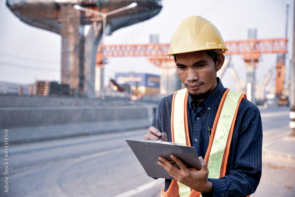 An engineer is reviewing an elevated road construction project. The engineer holds a file for working on the road construction site. An engineer is reviewing an elevated road construction project. The engineer holds a file for working on the road construction site.