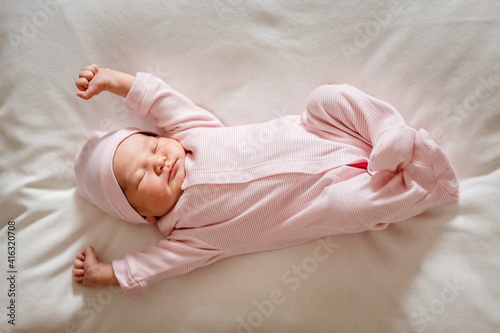 Cute little girl of 5 days in a pink jumpsuit lie on plaid and stretches in a dream in full height