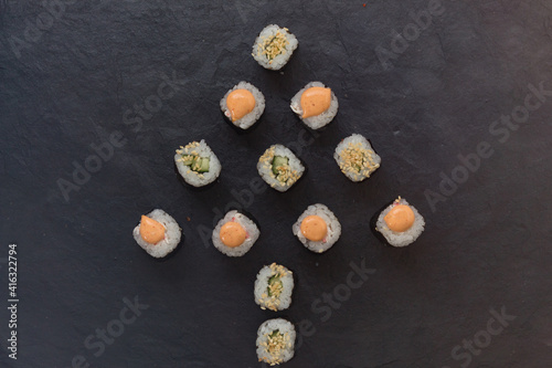 mini rolls are lined with Christmas trees on a black stone platter. Rice, cucumber, sesame, avocado, nori