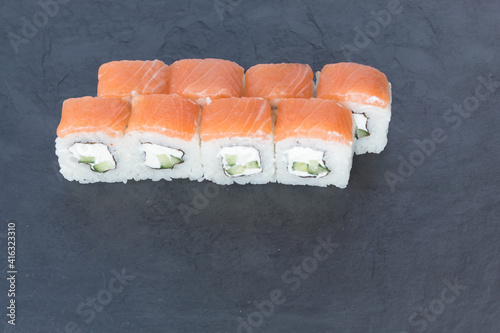 Rolls with salmon on a black stone board. Serve the dish. Rice, fish, avocado.