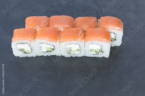 Rolls with salmon on a black stone board. Serve the dish. Rice, fish, avocado.