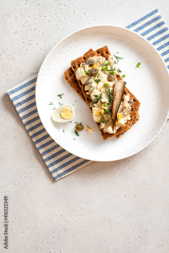 Egg salad with anchovies on crispy bread. Sandwich with Swedish egg salad gubbröra in a plate on a white concrete background top view. Scandinavian cuisine. Copy space for text