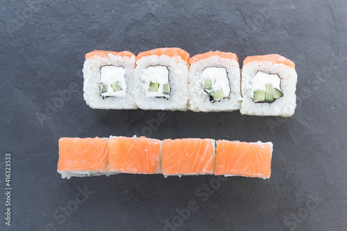 Rolls with salmon on a black stone board. Serve in 2 rows. one row on top, the other in section
