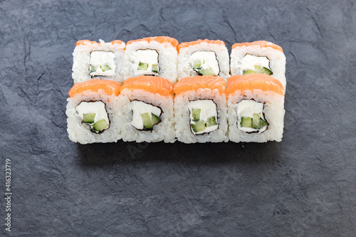 Rolls with salmon on a black stone board. Serve a cutaway dish. Rice, avocado, salmon