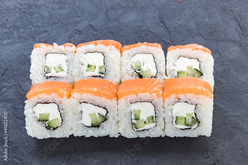 Rolls with salmon on a black stone board. Serve the dish. Rice, fish, avocado.