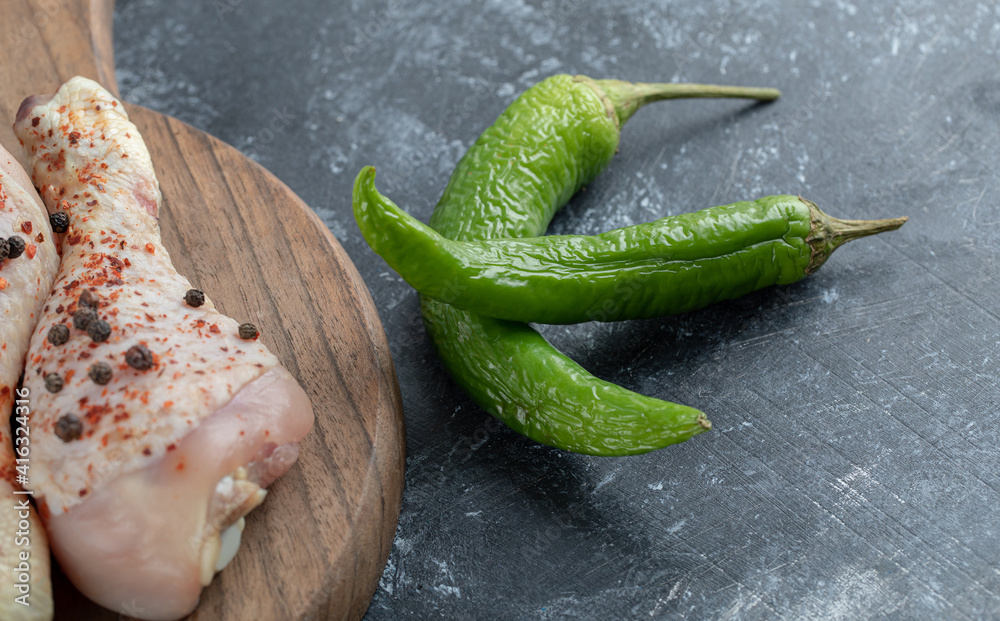 Fresh organic chicken drumsticks and green pepper on wooden chopping board Fresh organic chicken drumsticks and green pepper on wooden chopping board