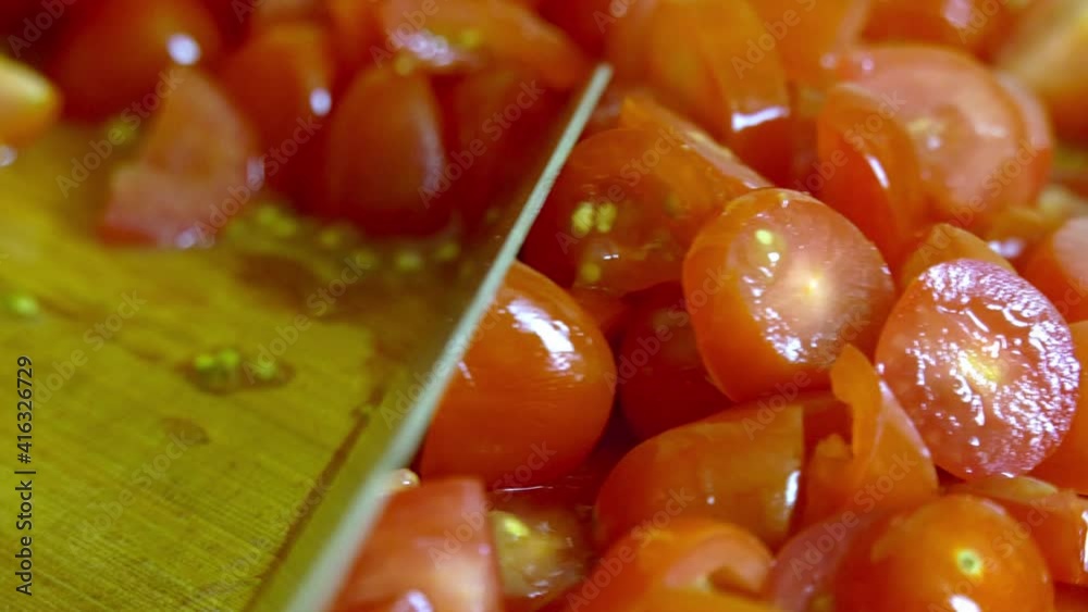 Red slices of cherry tomatoes being scraped with a silver knife on a wooden cutting board. Close up shot Red slices of cherry tomatoes being scraped with a silver knife on a wooden cutting board. Close up shot