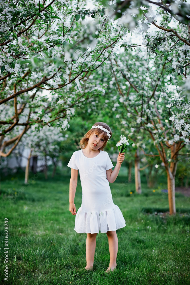 Cute kid girl 5-6 year old holding flower standing in blossom spring garden Cute kid girl 5-6 year old holding flower standing in blossom spring garden