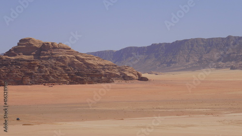 Einsamer Jeep fährt durch die Wüste Wadi Rum, im Hintergrund Filmkulisse Lawrence von Arabien