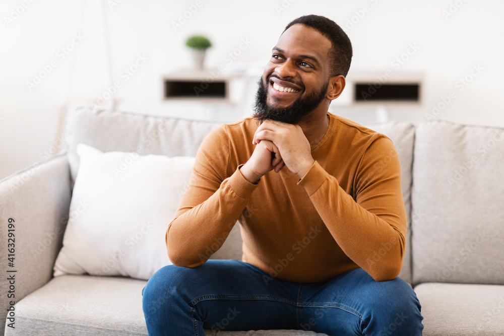 Happy African Guy Thinking Dreaming Sitting On Sofa At Home