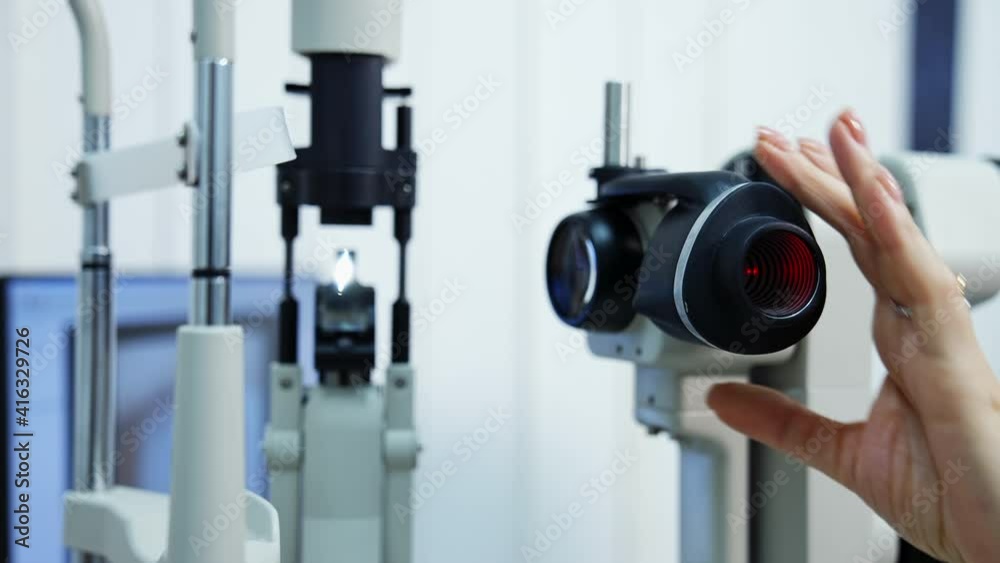 Panning shot of female ophthalmologist`s hand doing eye exam with slit lamp. Preparing special technic for checking eyesight. Selective focus. Panning shot of female ophthalmologist`s hand doing eye exam with slit lamp. Preparing special technic for checking eyesight. Selective focus.