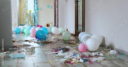 Scared, surprised cat walks on wooden laminate after party chaos, messy in living room at home, confetti and balloons, morning after party celebration.