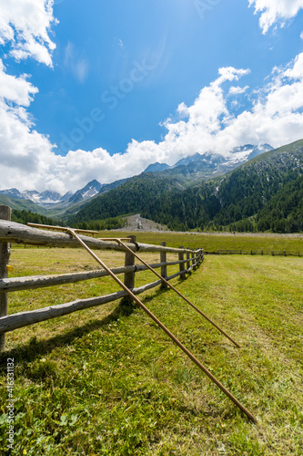 two agricultural tools on a wooden fence on a alpine pasture with high mountains