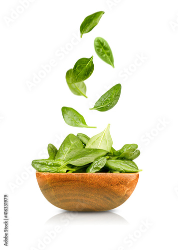 isolated spinach leaves falling into a wooden plate. isolated on white background