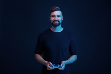 Young man in black t-shirt with joystick in hands playing in video games. Dark background. Guy enjoying victory and expresses happiness. Blue neon light.