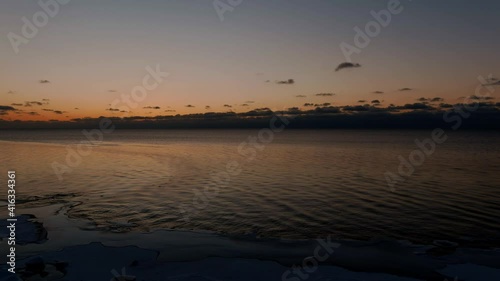 Sunset in a calm sea with frozen seashore. Shot from drone