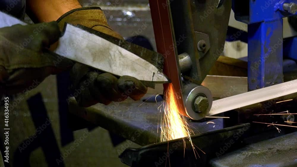 Male wearing his personal protective equipment on a grinding machine to grind the top of the knife he is making while sparks flying around. Close up shot