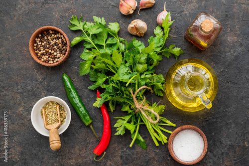 Prepared ingredients for Chimichuri, Argentinean green steak sauce with fresh parsley, garlic, olive oil and oregano on a dark concrete background. Sauce recipes.