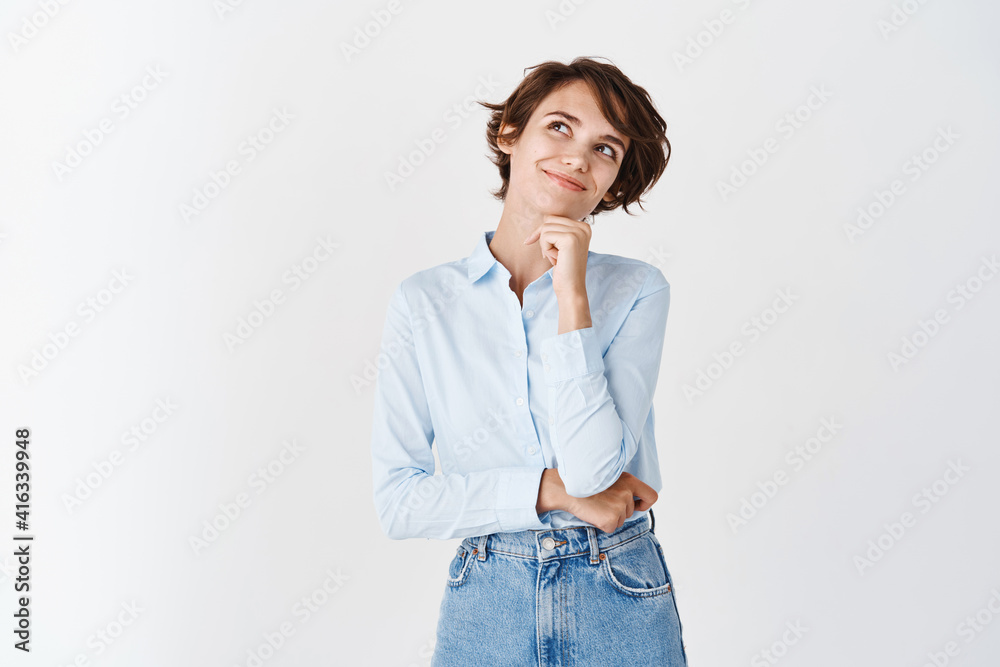 Dreamy young girl student looking at upper left corner, smiling and imaging things, standing in blue collar shirt on white background Dreamy young girl student looking at upper left corner, smiling and imaging things, standing in blue collar shirt on white background