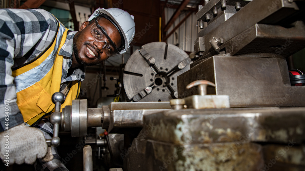 Africa American worker wearing safety goggles control lathe machine to drill components by wrench. Metal lathe industrial manufacturing factory indoors. Sander concept.