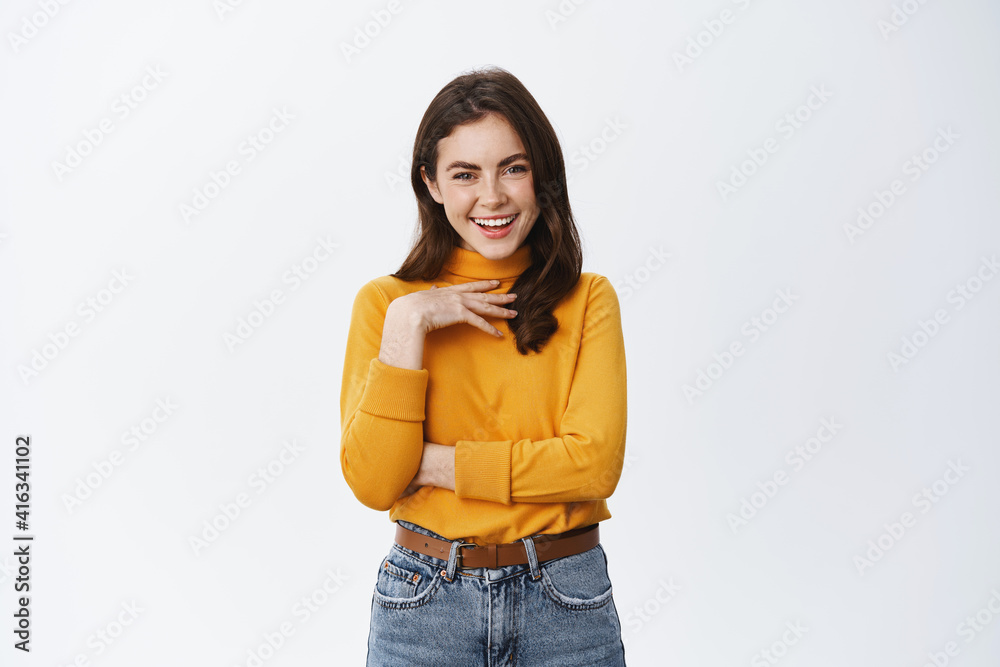 Happy confident woman laughing, touching chest and pointing at herself self-appreciation gesture, standing in yellow jumper against white background Happy confident woman laughing, touching chest and pointing at herself self-appreciation gesture, standing in yellow jumper against white background