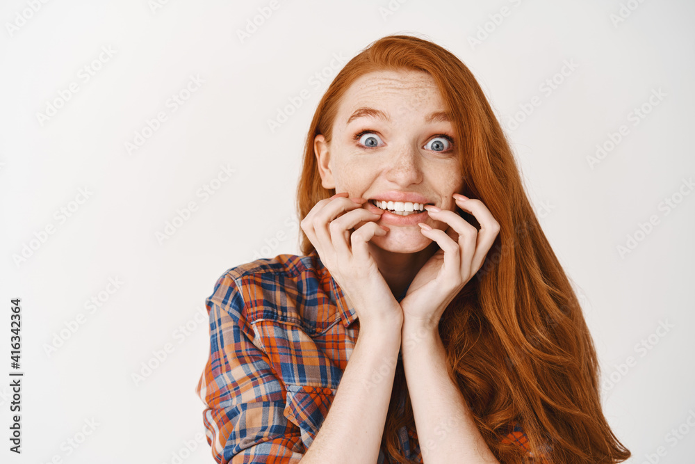 Close-up of excited redhead woman rejoicing of great news, smiling happy and staring at camera, standing against white background Close-up of excited redhead woman rejoicing of great news, smiling happy and staring at camera, standing against white background