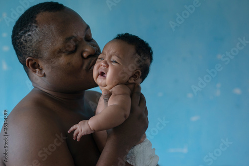 African father holds his baby girl on blue background, 4 mouth baby, man is not wearing a shirt