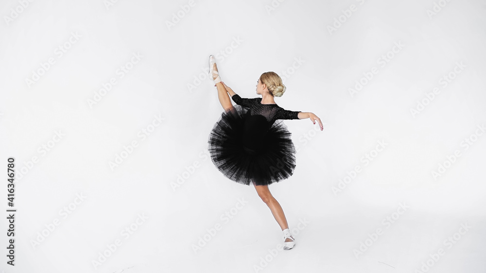 flexible ballerina in tutu skirt and pointe shoes stretching while dancing on white background