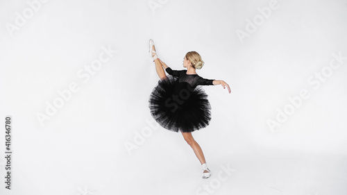 flexible ballerina in tutu skirt and pointe shoes stretching while dancing on white background