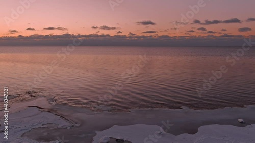 Sunset in a calm sea with frozen seashore. Shot from drone