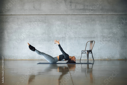 Full-length female yoga instructor, doing difficult Uttana Padasana pose on a mat on the floor of a urban industrial big sunny gymnasium, with gray concrete walls, modern fitness pilates studio. photo