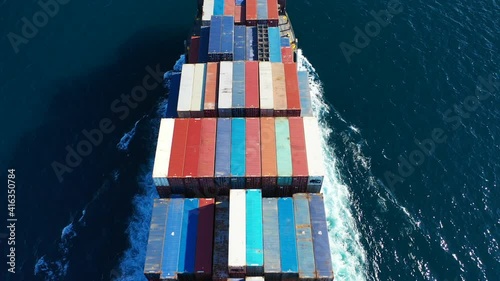 Aerial top down video of Container cargo Ship carrying load in truck-size colourful containers in deep blue open ocean sea 