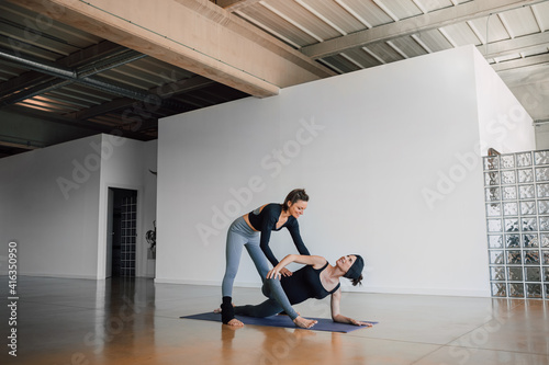 Pregnant woman taking prenatal classes from a female Personal yoga coach  who helps to make a twist pose  stretching  in a big gymnasium. Fitness workout healthy lifestyle concept.